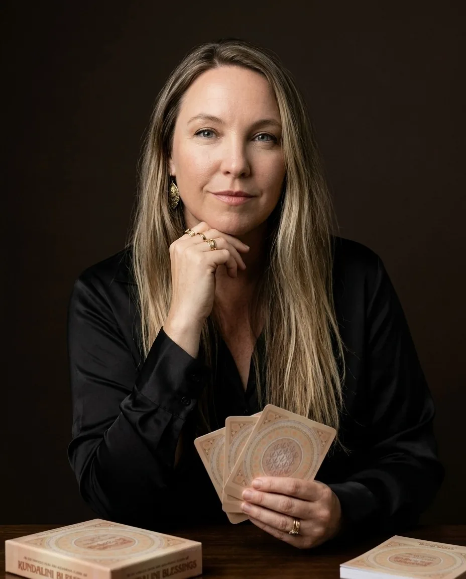 Gurudarshan in a black shirt, hand at her jaw, holding a fan of Kundalini Blessings cards